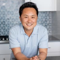 Leon Chen wearing a blue button up shirt, smiling in a kitchen